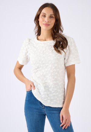 Top bianco a maniche corte con motivo testurizzato e leggere maniche a sbuffo; tessuto morbido e vestibilità rilassata, abbinato a jeans in denim blu.