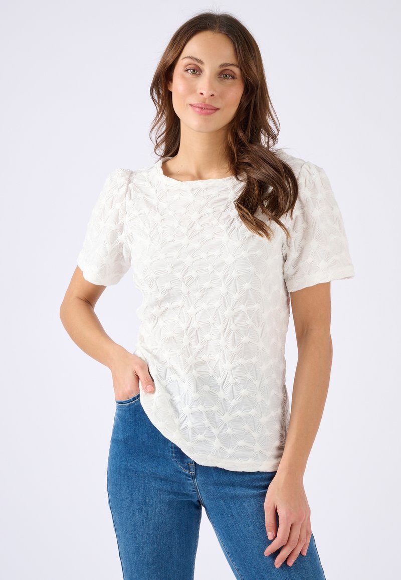 Witte korte mouw top met textuurpatroon en lichte puff-mouwen; zachte stof en relaxed fit, gecombineerd met blauwe denim jeans.