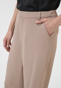 Beige op maat gemaakte broeken met een gladde textuur, voorzien van zijzakken en subtiele plooien bij de taille voor een gestructureerde pasvorm.
