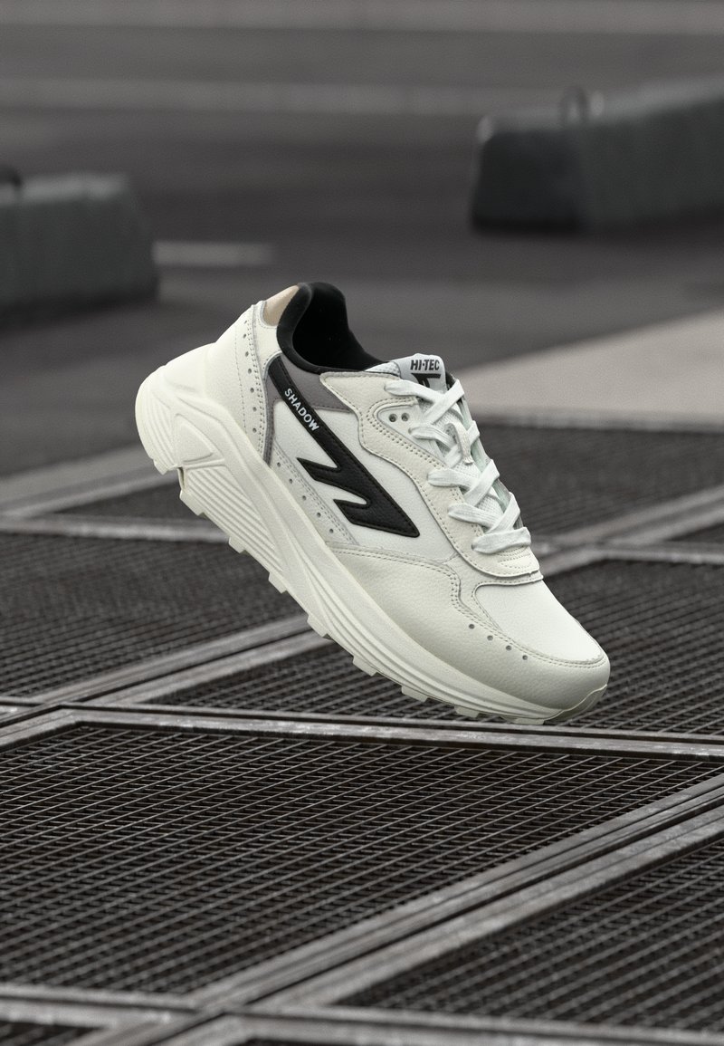 Adidași din piele albă cu un accent negru, cu un superior texturat, talpă groasă și detalii perforate. Beneficiază de o guler căptușit și shoelaces.