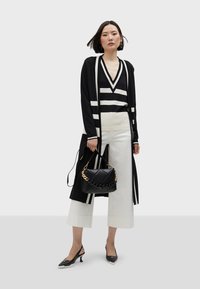 Svart- och vitrandig kavaj över en v-ringad topp, kombinerad med vida vita byxor och svarta slingbackklackar med spetsig tå. Svart vadderad handväska.