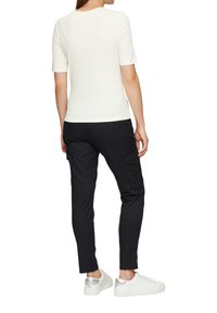 Weißes Kurzarmoberteil, kombiniert mit schwarzen Cargo-Hosen mit Taschen. Das Outfit wird durch weiße Sneakers mit silbernen Akzenten abgerundet.