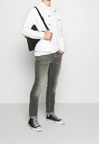 Vit jeansjacka, vit t-shirt, grå jeans, svarta sneakers. Slim fit, avslappnad design med kontrastsömmar och uppvikta byxben.