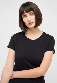 T-shirt noir à manches courtes en tissu doux avec un col rond et un logo subtil sur la poitrine. Texture lisse, coupe ajustée.