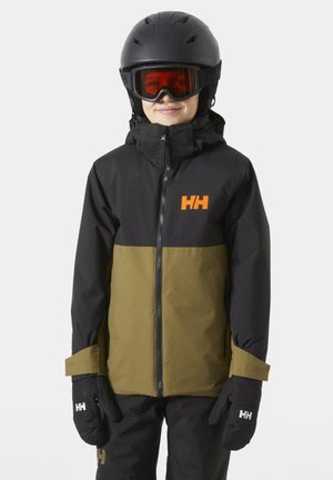 Bambino che indossa una giacca da sci nera e oliva, casco nero, occhiali da sci arancioni e guanti neri, in piedi davanti a uno sfondo semplice.