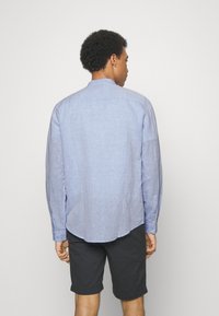 Camisa de manga larga azul clara con cuello abotonado, tela texturizada y dobladillo curvo, combinada con pantalones cortos oscuros.