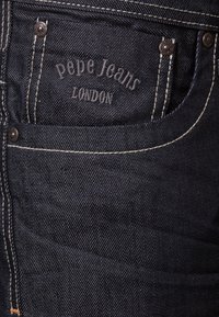 Mörkblå denimjeans med synliga sömmar, en framficka som visar den präglade "Pepe Jeans London"-logotypen och metallnit.