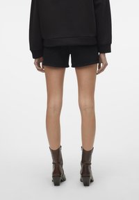 Svarta jeansshorts med rak skärning och minimal detaljer, tillsammans med glänsande bruna klackstövlar och en löst sittande svart sweatshirt.