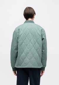 Ανοιχτό πράσινο καπιτονέ μπουφάν με στρογγυλεμένο γιακά, ριμπ μανσέτες και υφασμάτινο μοτίβο σταγόνων νερού.