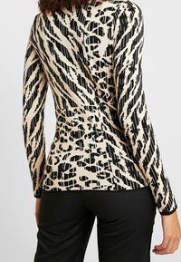 Maglia a maniche lunghe con motivo beige e strisce e macchie astratte nere, caratterizzata da un design aderente e una texture a costine lungo i polsini e l'orlo.
