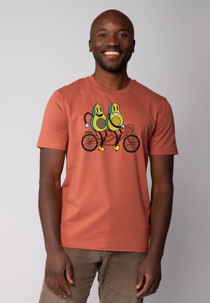 Rustkleurig t-shirt met een grafiek van twee avocado's die op een tandemfiets rijden. Gemaakt van zachte stof met een klassieke pasvorm.