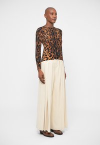 Leopardmönstrad stickad tröja med långa ärmar, i kombination med högmidjade, veckade beige byxor. Bruna skor fulländar looken.