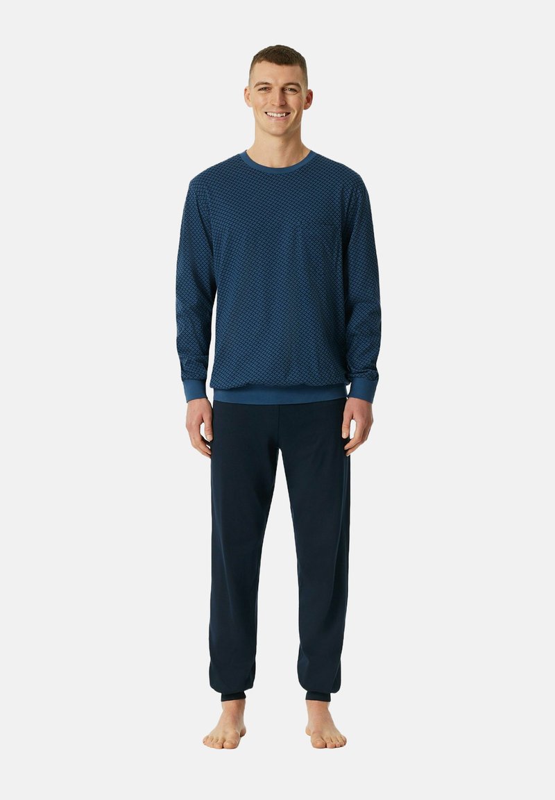 Navy blue loungewear-setti, jossa on pitkähihaista kuviollista paitaa ja yksivärisiä housuja, molemmat pehmeää kangasta ja joustavia hihansuissa, käytettynä paljain jaloin.