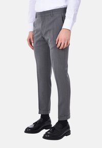 Pantaloni grigi su misura con una texture liscia, pieghe davanti e risvolti alle caviglie, abbinati a mocassini neri e calzini.