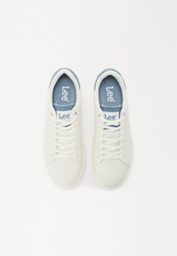 Baskets blanches avec un dessus en cuir lisse, accents bleu clair au col et à la semelle intérieure, avec un design à lacets et un logo sur la languette.