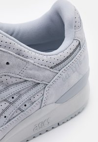 Gray suede sneaker with perforated detailing, contrasting light gray accents, and a thick rubber sole. Features "ASICS" branding on the side.