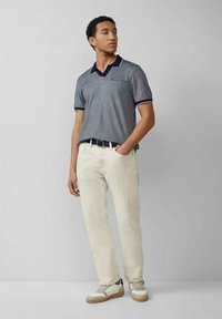 Graues Poloshirt mit kontrastierendem navyfarbenem Kragen und Tasche, kombiniert mit cremefarbenen Hosen und hellen Sneakers. Schlichte, legere Gestaltung.