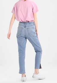 Camiseta de color rosa claro combinada con jeans de tiro alto en azul. Los jeans tienen franjas laterales y un ajuste slim, mientras que los zapatos son zapatillas blancas.