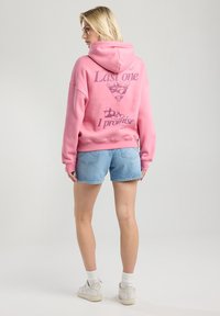 Pink sweatshirt with hood, featuring a graphic of a martini glass and text: "Last one I promise." Paired with light blue denim shorts.