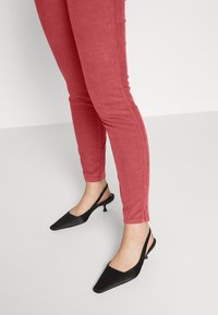 Pantaloni slim-fit in corduroy rossi abbinati a scarpe slingback con tacco kitten nero e punta affusolata. Design semplice, superficie liscia e dettagli minimali.