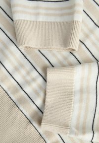 Tessuto a maglia a righe beige e bianche con accenti marrone scuro. Presenta polsini a coste e una texture liscia, mettendo in evidenza schemi a righe alternate.
