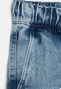 Tessuto di denim azzurro chiaro con una vita arricciata. Presenta cuciture in vista e una texture leggermente scolorita. Progettato per comfort e facilità.