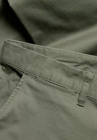 Olivgrüne Hosen aus glattem Baumwollstoff. Enthalten einen flachen Bund, Gürtelschlaufen und sichtbare Nähte entlang der Säume.