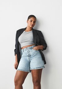 Svart smalrandig blazer över en grå ribbad crop top, tillsammans med högmidjade ljusblå denimshorts med fransad nederkant.