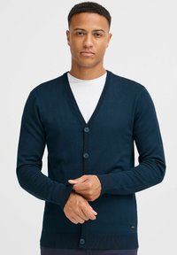 Námornícky modrý pletený cardigan s V-výstrihom, päťgombíkovým zapínaním, rebrovanými manžetami a lemom, vyrobený z mäkkého, štruktúrovaného materiálu.