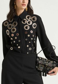 Blusa nera con decorazioni circolari metalliche e paillettes, abbinata a una piccola borsa nera con perline con motivi floreali e nappina.