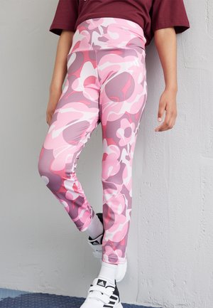 Leggings de tejido elástico, con un patrón floral en tonos rosa y morado, cintura alta y una silueta ajustada. Combinados con zapatos negros.