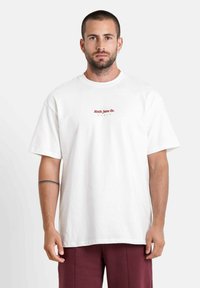 Witte katoenen t-shirt met korte mouwen, voorzien van een rood logo tekst "North Jane Co. PARIS" in het midden. Eenvoudig design, relaxte pasvorm.