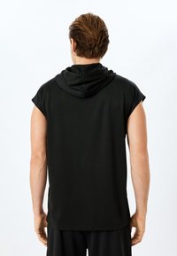 Zwarte mouwloze capuchonshirt gemaakt van gladde stof, met een relaxte pasvorm en vlakke naden. De achterkant heeft een eenvoudig, onversierd ontwerp.