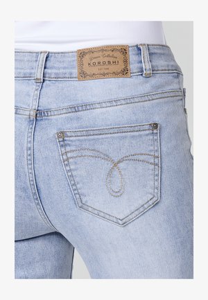 Heledad sinine teksapüksid, mille tagaküljel on nahklabel. Omavad kuldseid õmblusi ja ainulaadset tasku kujundust styliseeritud mustriga.