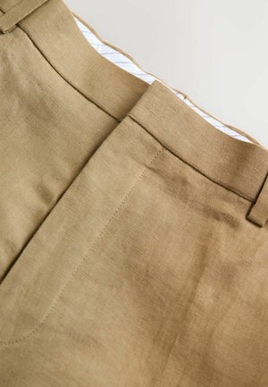 Pantalons en lin beige clair avec une texture lisse, présentant un devant plat, une taille et des détails de couture subtils. La doublure intérieure comporte de légères rayures.