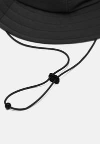Sort bucket hat lavet af tekstureret stof, med en bred skygge og en justerbar elastisk snor med en stopper for en sikker pasform.