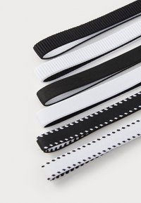 Set van zes haarbandjes in zwart en wit. Kenmerken omvatten een ribbelstructuur, een gladde afwerking en contrasterende kleuren met subtiele stikdetails.