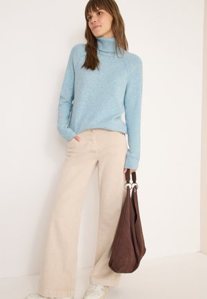 Lichtblauwe coltrui met ribbelstructuur, gecombineerd met beige wijde broek. Model houdt een donkerbruine suède tas vast.