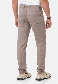 Gestreifte braune Hose mit schmaler Passform, mit Gesäßtaschen und sichtbarem Bund, kombiniert mit beigefarbenen Sneakers auf einem weißen Hintergrund.