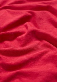 Roter Stoff mit einer glatten, leicht strukturierten Oberfläche, der über sanfte Falten und Knicke verfügt, was auf ein leichtes und atmungsaktives Material hinweist.
