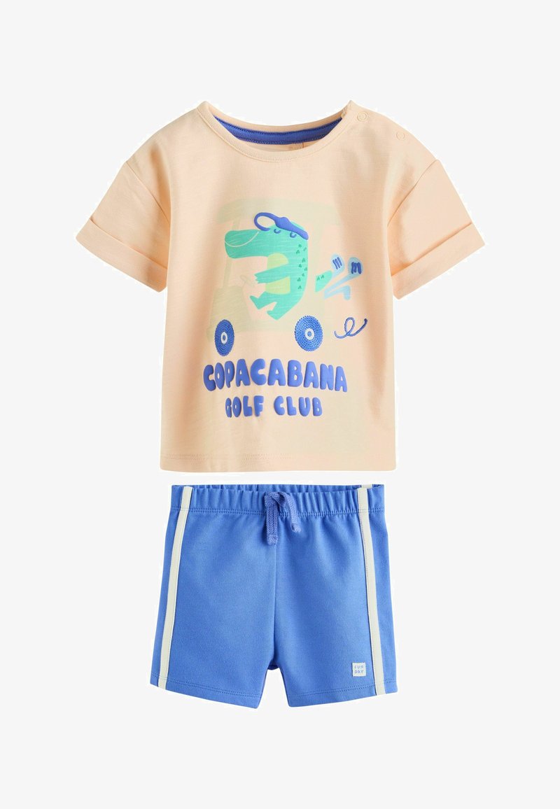Chemise beige à manches courtes pour tout-petit avec un dinosaure bleu sur une voiturette de golf et le texte "Copacabana Golf Club", associée à un short bleu à rayures blanches.
