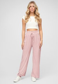 Pantalons larges côtelés rose clair avec une taille élastique et un détail de cordon de serrage. Associés à un crop top blanc ajusté et des baskets blanches.