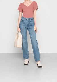 Geribbelde roze top met een V-hals, gecombineerd met lichtblauwe hoge rechte jeans. Bevat een beige handtas en roze schoenen.