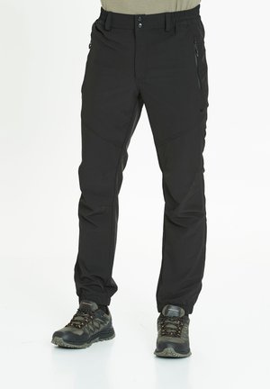 Black outdoor pants with a slim fit, made of durable fabric, featuring zippered pockets and adjustable cuffs. Worn with black hiking shoes.