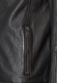 Schwarze Lederjacke mit einer auffälligen Reißverschlusstasche auf der linken Seite, mit einer strukturierten Oberfläche und glatter Verarbeitung.