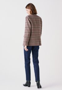 Bruin geruit blazer met notch lapels, lange mouwen en enkele rugventilatie, gecombineerd met donkerblauwe aansluitende jeans en zwarte haklaarzen.