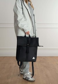 Mochila negra de tipo roll-top hecha de material impermeable, con un bolsillo frontal con cremallera, correas ajustables y un logotipo triangular.