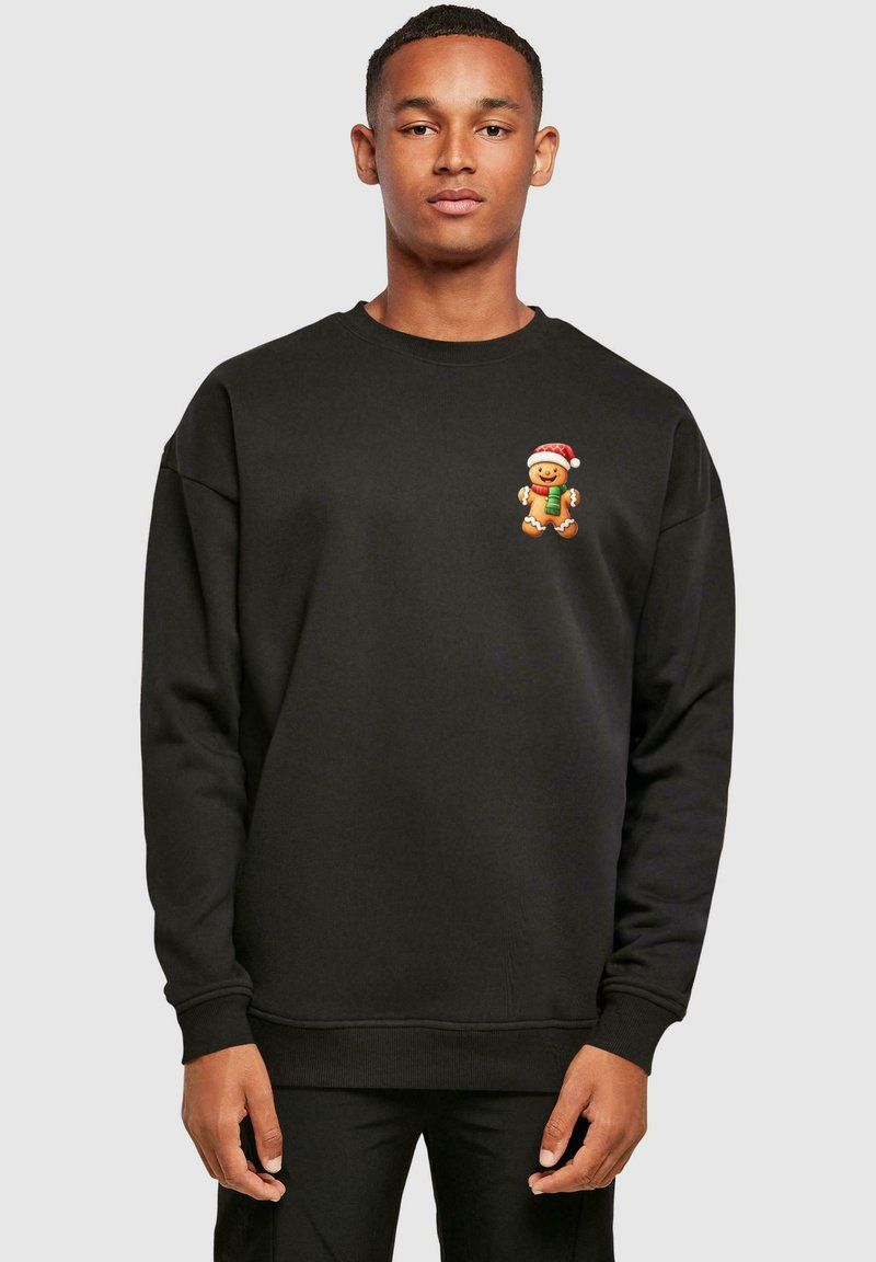 Sort sweatshirt med rund hals, der har et ingefærbrød karakter iført en julehue og holder en gave på brystet.