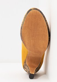 Chaussure avec une tige en daim jaune, des accents texturés à motif animal, et une semelle en caoutchouc brun à finition lisse.
