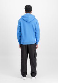 Modra kapuca s vrvico in rebrastimi manšetami, v kombinaciji z črnimi cargo hlačami, ki imajo stranske žepke in ohlapen kroj.